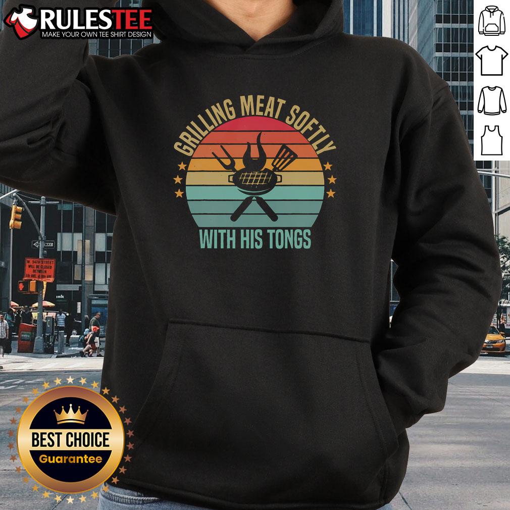 Man in a vintage barbecue hoodie grilling meat softly with tongs at an outdoor barbecue, showcasing awesome grilling skills.