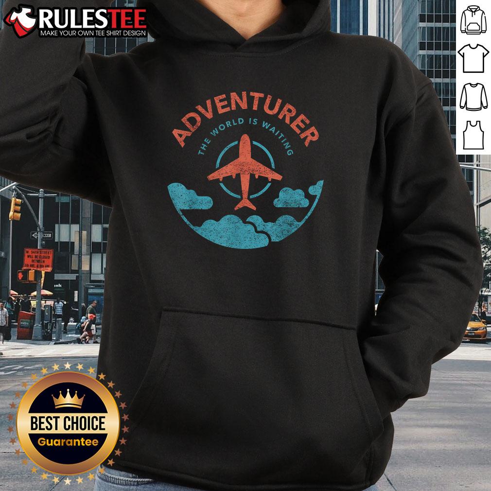 Funny adventurer wearing a 'The World Is Waiting For Travelers' hoodie next to a plane, ready for travel adventures.