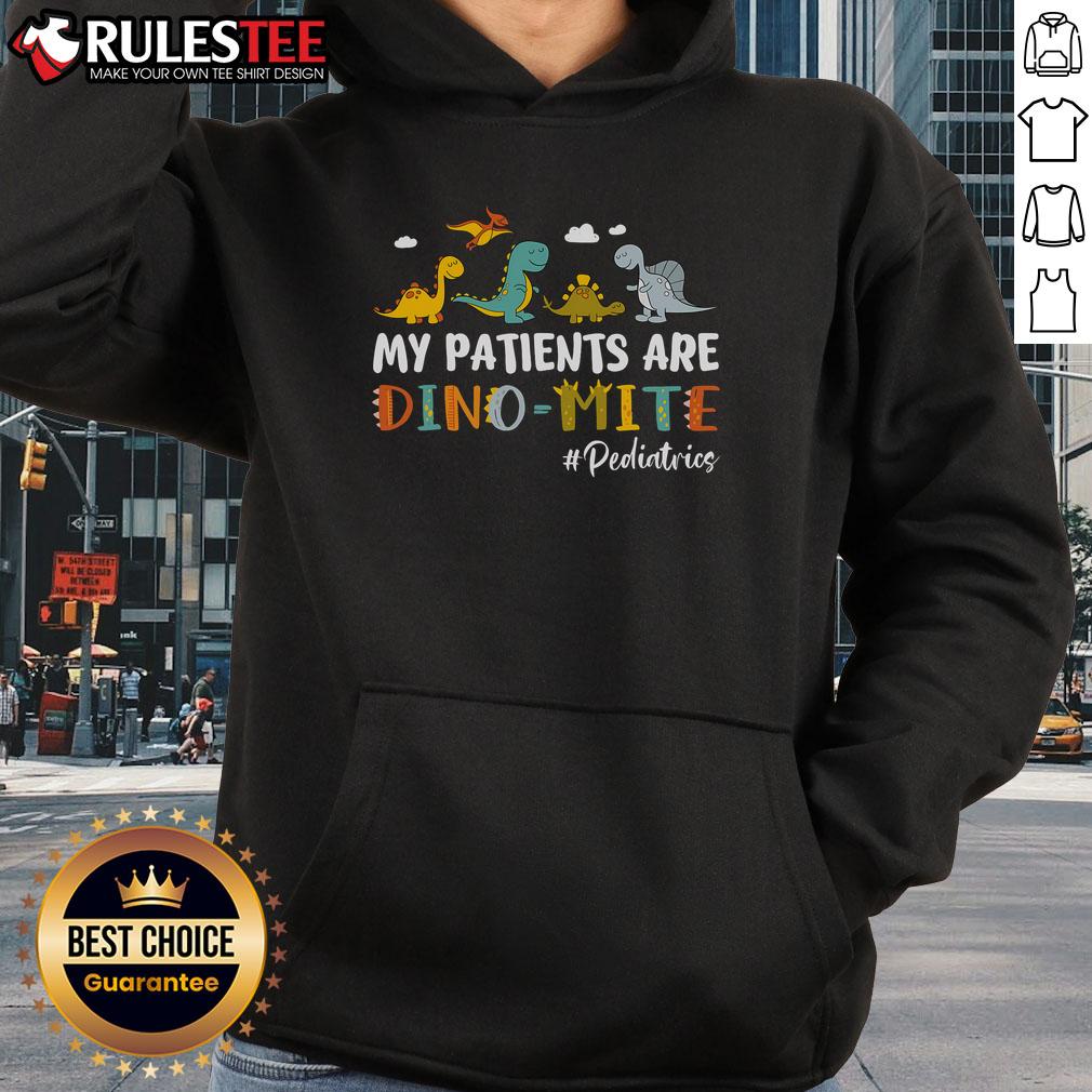 Cute pediatric nurse wearing a dinosaur hoodie that says 'My Patients Are Dino-Mite' in a colorful hospital setting.
